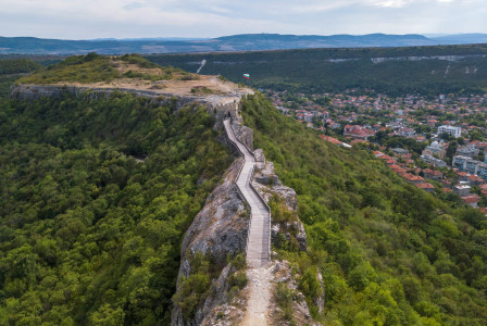 An illustrative photo of a brown wooden bridge on mountain peak near cityscape.