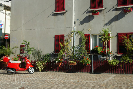 An illustrative photo of a scooter parked in front of a building with red shutters.