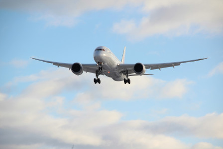 An illustrative photo of a white passenger plane in mid air during daytime.