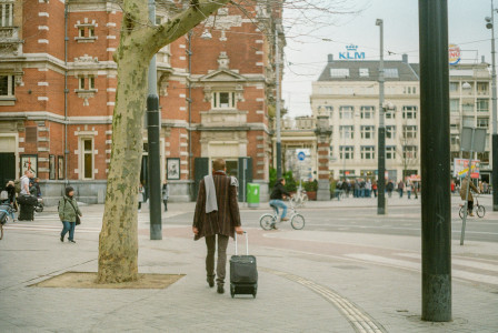 An illustrative photo of a woman walking on a street while carrying a suitcase.