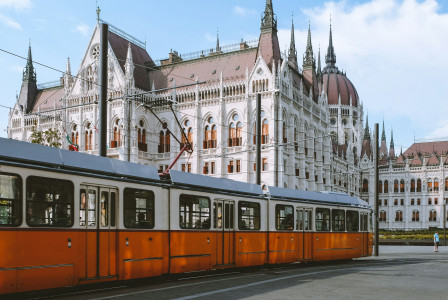 An illustrative photo of an orange and white tram near the Hungarian Parliament.