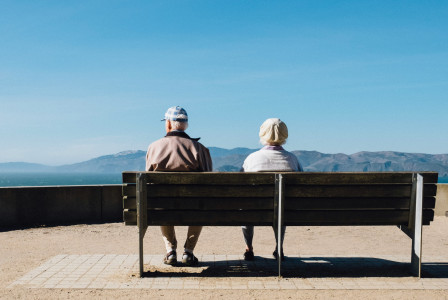 An illustrative photo of a man and a woman sitting on a bench facing sea.