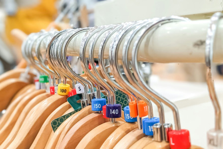 Close-up view and selective focus of empty wooden hangers with colorful plastic size tags.