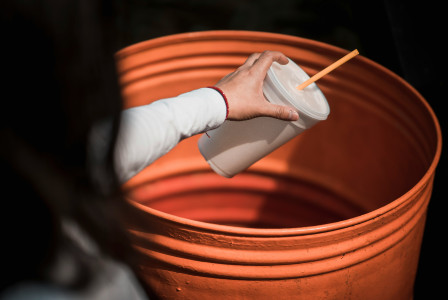 An illustrative photo of a person throwing away a paper cup.