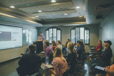 An illustrative photo of a group of people in a room with a projector screen.