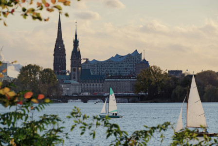 An illustrative photo of a white sail boat on water near city buildings.