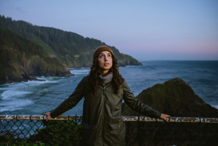 An illustrative photo of a woman standing on a fence near the ocean.