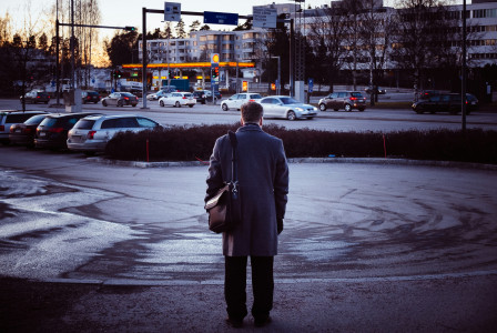An illustrative photo of a man in black coat standing on sidewalk.