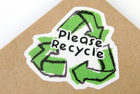 Recycle symbol with the words “Please Recycle” printed on a cardboard background.