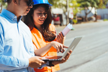 Civil engineer and architect wearing blue safety helmet meeting at construction site
