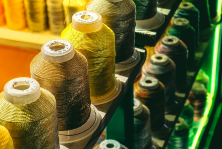 Colour photograph of a row of spools of thread resting on a shelf