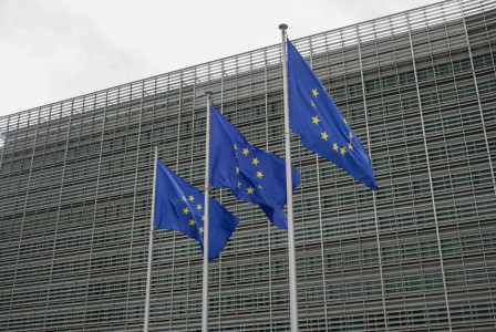 Three European flags flying in front of a building. 