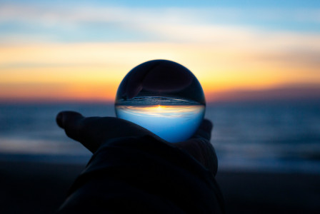 Person holding a glass ball with sunset at the horizon