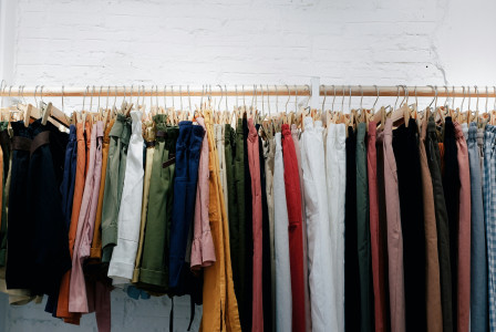 Clothing rack with colorful pants on wooden hangers against a white brick wall