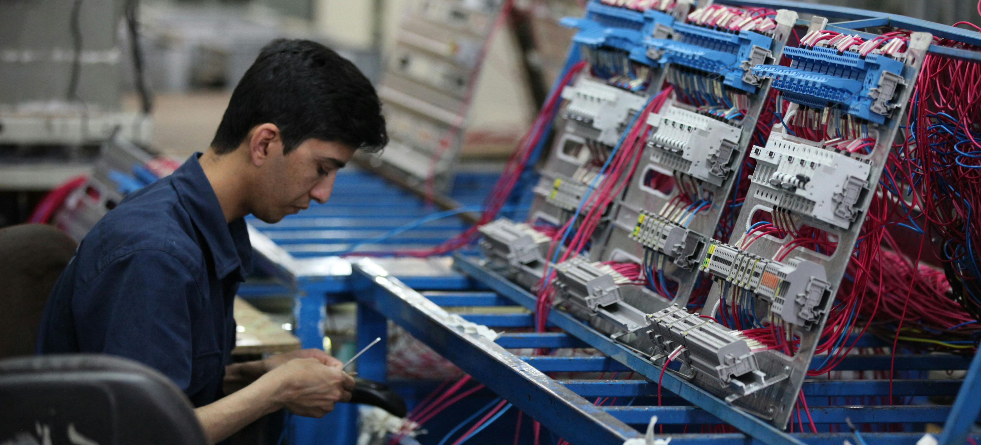 A photo presenting a technician wiring an electrical control panel on a factory assembly line.