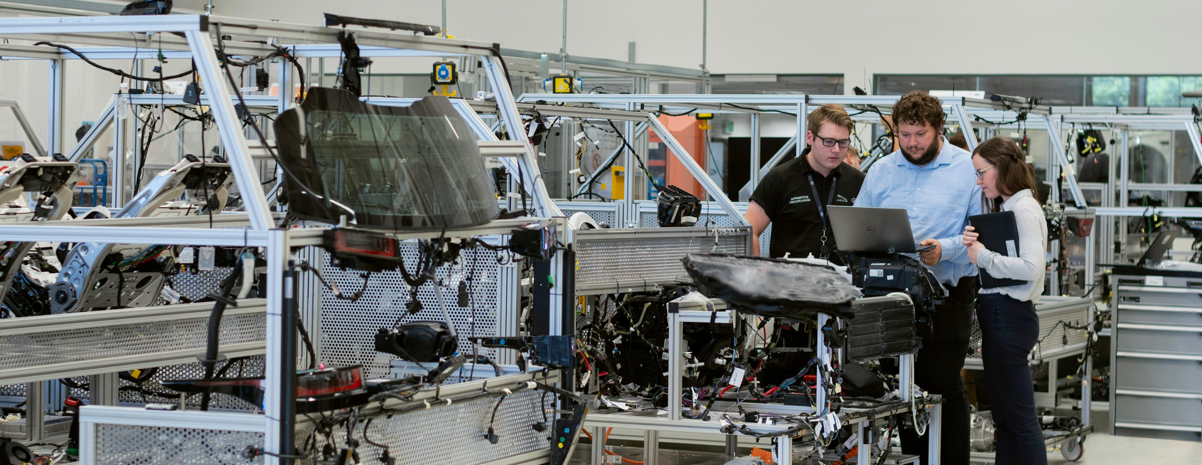 A photo presenting engineers reviewing data on a laptop in an automotive assembly workshop.