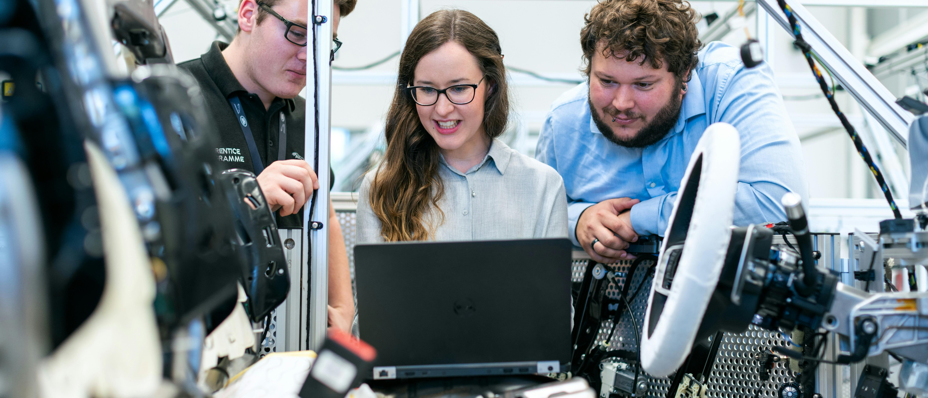 A photo presenting three engineers discussing data on a laptop at an automotive test rig.