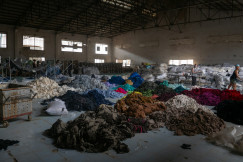 Sorted piles of colourful fabric waste inside a large industrial warehouse.