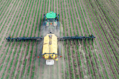A photo representing a tractor applying fertiliser across a cultivated field.
