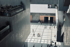 A spacious indoor atrium with geometric shadows and people walking by.