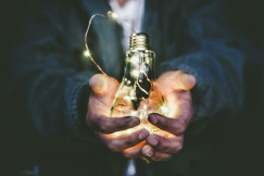 Colour photograph of a man holding a lit light bulb in his hands, close-up of the hands and light bulb by Riccardo Annandale on unsplash