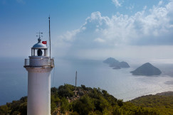 white-and-brown-lighthouse-near-green-trees-under-white-clouds-and-blue-sky