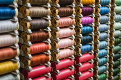 Close up view of multiple colourful thread spools arranged on shelves, representing textile manufacturing, yarn production and material diversity within the textile industry.