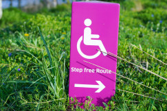Photo presenting a purple "Step free Route" sign with a wheelchair symbol, set among green grass.