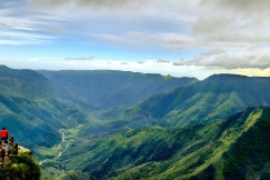 Photo presenting visitors at a lookout point overlooking a lush green river valley in the mountains.
