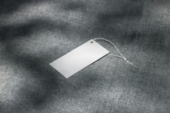 Blank clothing tag resting on a grey textile fabric surface.