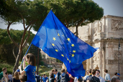 A young girl holding a European flag in front of a crowd of people .