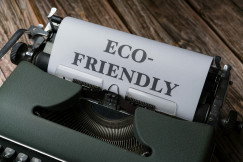 Photo presenting a vintage green typewriter on a wooden surface, with a sheet of paper rolled into it reading "ECO-FRIENDLY" in bold typed letters.