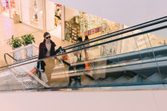 A photo presenting a woman with shopping bags riding an escalator in a shopping centre.