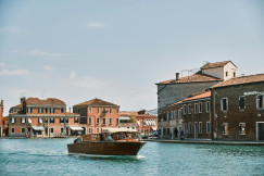 A picture presents a boat traveling along a canal beside historic buildings.