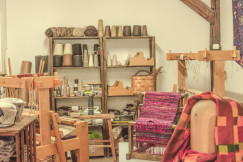 Wooden weaving workshop with looms, yarn spools, and a woven textile in progress.