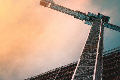 A photo presents a construction crane beside a tall building.