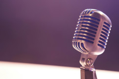 Photo presenting a vintage microphone on a stand against a blurred purple background.