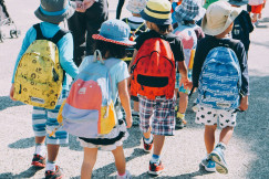 A picture presents children walking outdoors with backpacks