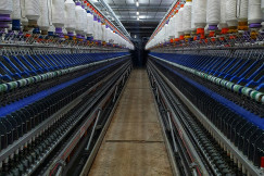 Industrial textile spinning machines with rows of yarn spools in a manufacturing facility, representing textile production, material innovation and sustainable industrial transformation.