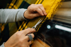 Close up of hands inspecting and trimming a woven textile fabric, demonstrating textile quality control, craftsmanship and material evaluation during fabric production.