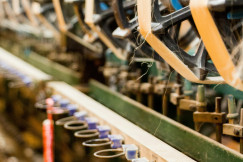 Close-up of textile manufacturing machinery processing yarn in an industrial spinning facility, representing textile engineering, material performance and research into durable textile products.