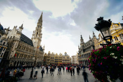 A picture presents a historic city square with grand buildings and people.