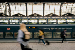 The photo presents people walking past a train at a station.
