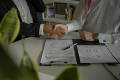 The photo presents two businesspeople shaking hands over signed documents, symbolising an agreement or partnership.