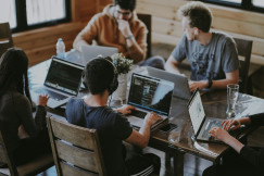 The photo presents a group of people working on laptops together.