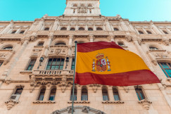 The photo presents the Spanish flag in front of a historic building.