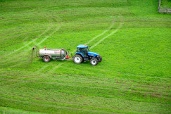 The photo presents a tractor working in a green field.