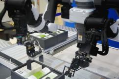 The photo presents industrial robotic arms handling products on an automated production line.