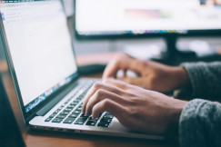 The photo presents a person typing on a laptop.