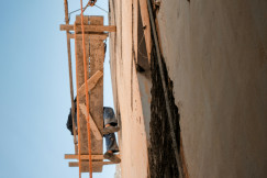 The picture presents a worker on a suspended scaffold beside a tall building wall.